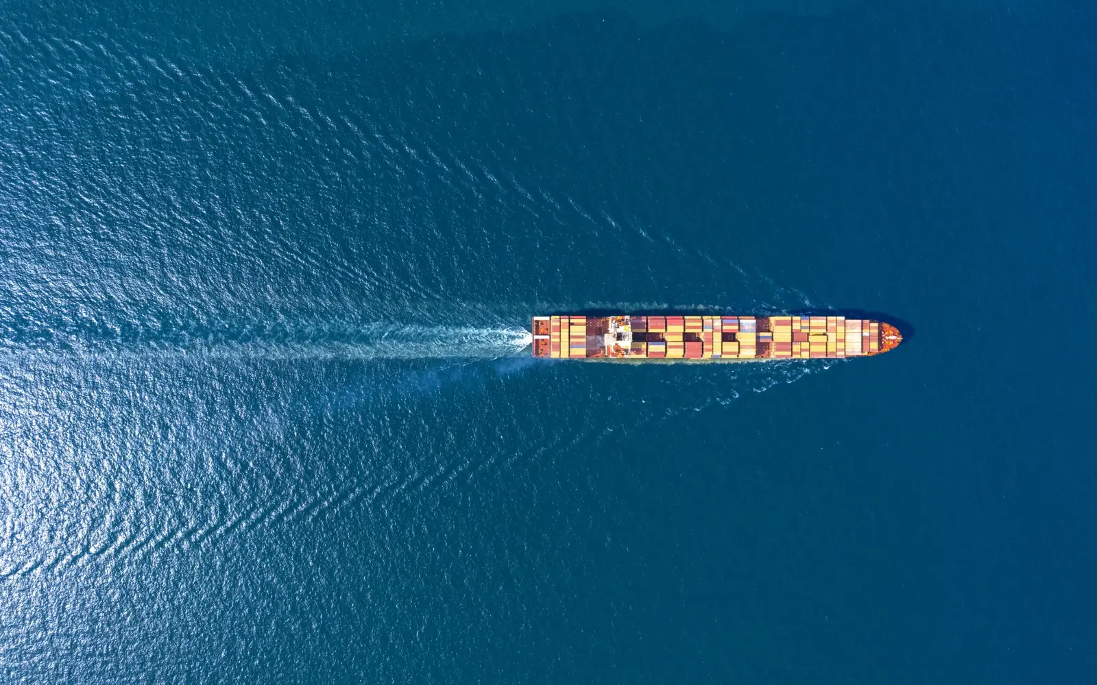 Aerial top-down view of a container ship crossing deep blue ocean