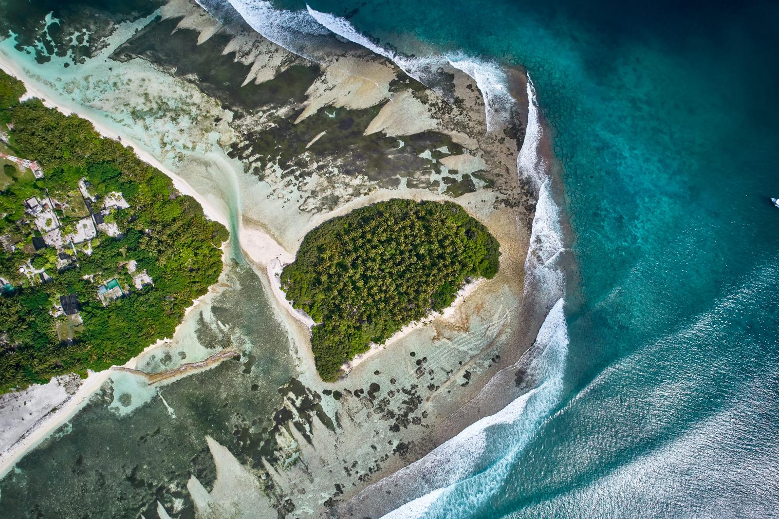 Top-down aerial of a palm island surrounded by reef and turquoise surf
